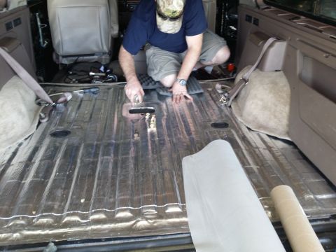 1994 Ford Bronco - A person works on applying soundproofing to the metal floor of a vehicle's interior.