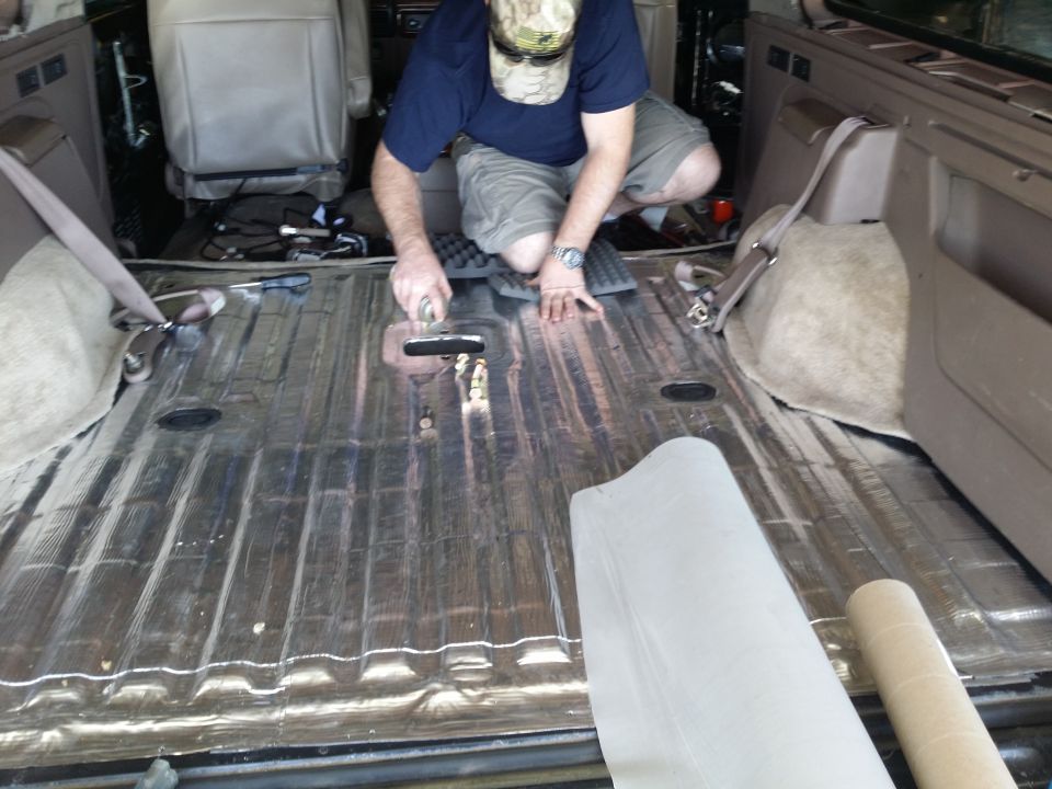 Interior of a vehicle with corrugated metal floor being covered with soundproofing material by a man