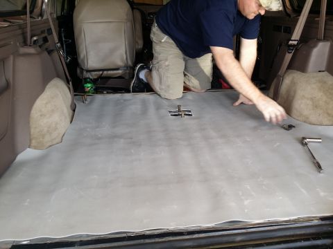 1994 Ford Bronco - Soundproofing material is being laid down in the rear cargo area of an SUV, with a socket wrench nearby.