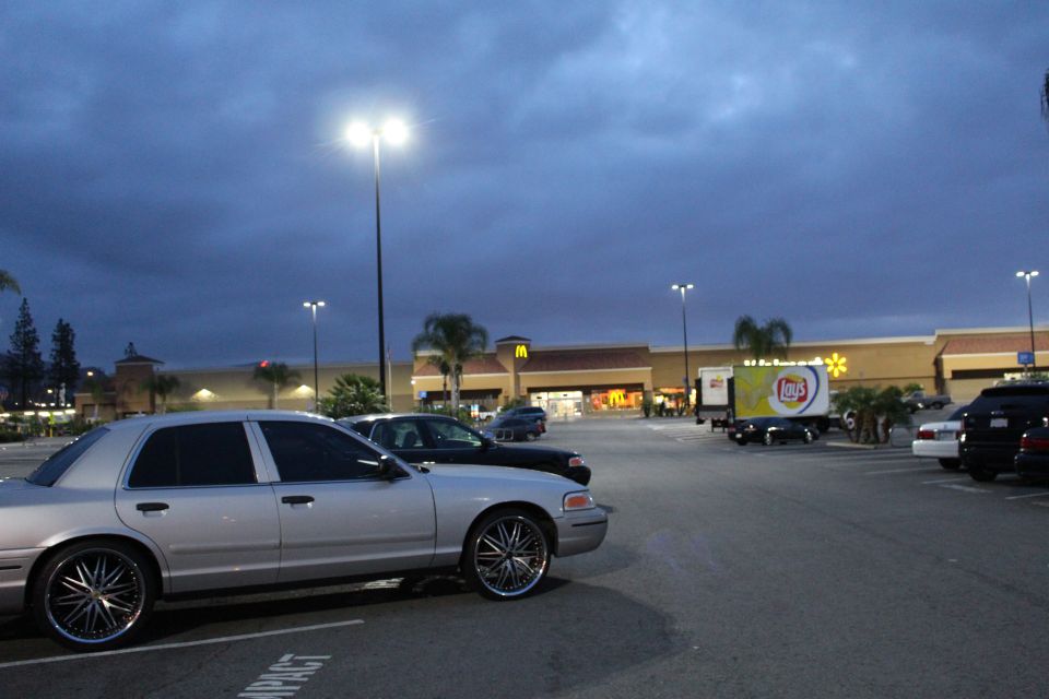Silver Ford Crown Victoria on chrome wheels parked at a shopping center lot at dusk