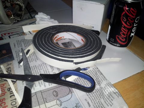 1976 Ford Ranchero - Foam weatherstripping tape and scissors are laid out on a surface with newspaper and a can of soda.