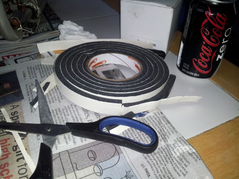 Roll of black foam weatherstripping tape with scissors and a can of Coca-Cola Zero
