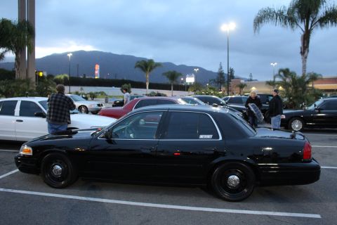 2003 Ford Crown Victoria - black Ford Crown Victoria with steel wheels and an INTERNET decal sits in profile in a strip-mall lot as people stand nearby at dusk.