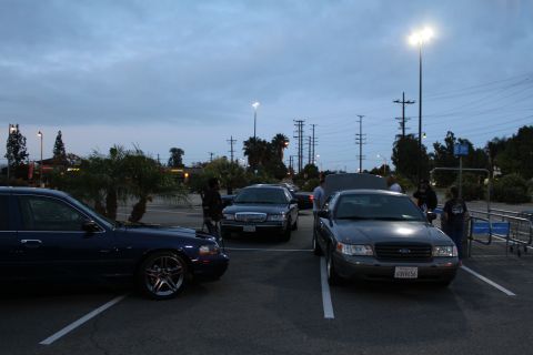 2003 Ford Crown Victoria - front of a Ford Crown Victoria and other full-size sedans sit in a dim parking lot at twilight with power lines overhead.