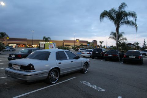 2003 Ford Crown Victoria - silver Ford Crown Victoria on chrome wheels parks rear-angled in a strip-mall lot near a McDonald's at dusk.