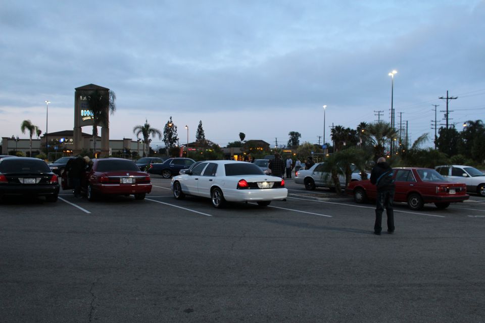 White Ford and other cars scattered across a wide parking lot at dusk