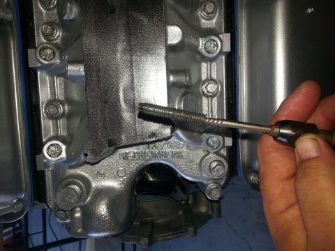 1994 Ford Bronco - A hand uses a tap tool on a metal engine component that has a Ford logo visible.