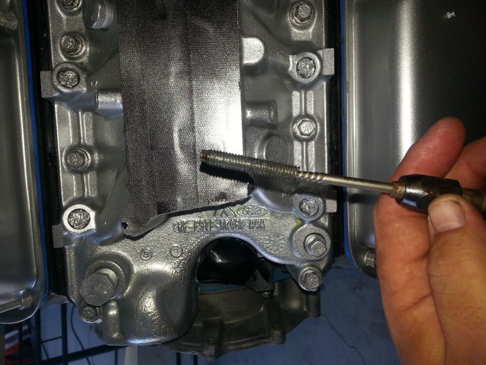 hand using tap tool on metal engine component with Ford logo