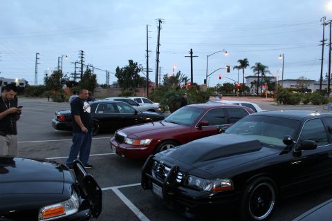 2003 Ford Crown Victoria - Black and dark red full-size sedans parked side by side at dusk, with two men standing nearby and power lines overhead.