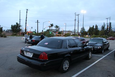 2003 Ford Crown Victoria - black full-size sedan viewed from the rear three-quarter with a paper plate, parked in a lot at dusk near a lit intersection.
