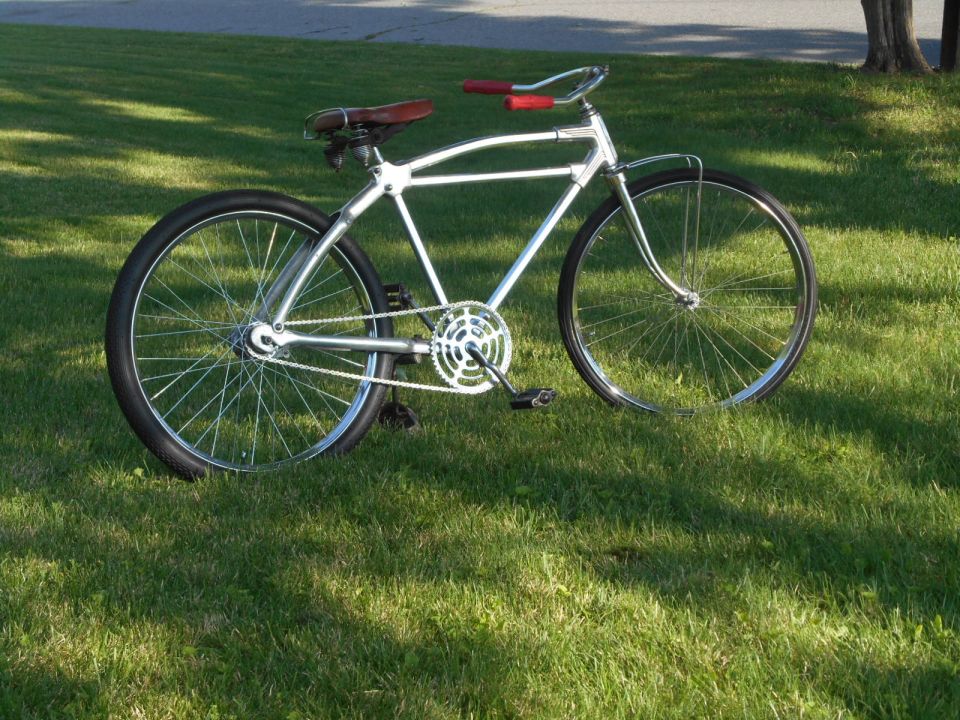 Chrome bicycle with red handlebars and a brown leather seat, parked on grass