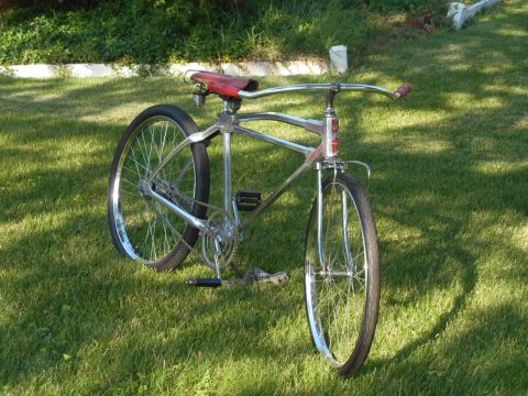 Chrome cruiser bicycle with red seat and handlebars, parked on grass