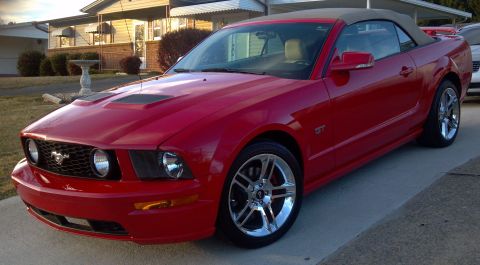 2006 Ford Mustang - A red convertible sports car is parked outside a house.