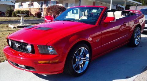 2006 Ford Mustang - Red convertible Ford Mustang with chrome wheels parked on a driveway.