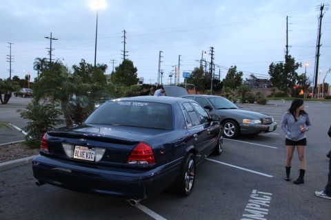 2003 Ford Crown Victoria - dark blue full-size sedan shown from the rear with a "BLUE VIC" plate and a rear-window banner, parked in a lot at dusk.