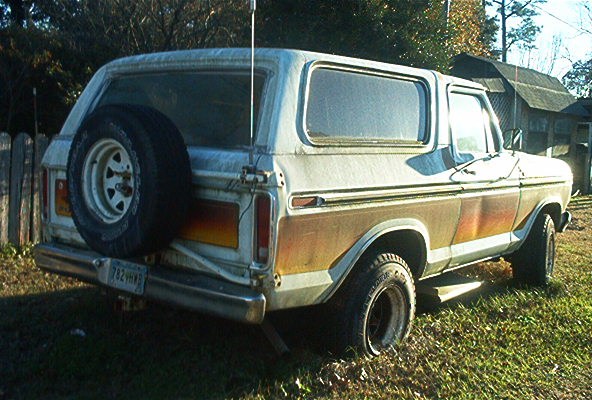 Rear three-quarter view of a white 1970s Ford Bronco with tailgate spare tire on grass