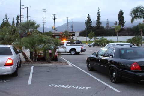 2003 Ford Crown Victoria - black full-size sedan and a white pickup truck parked in a lot marked COMPACT at dusk, with mountains and palm trees behind.