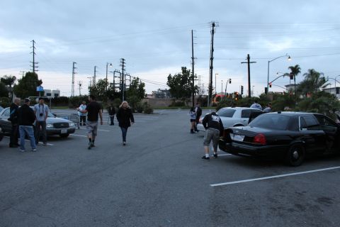 2003 Ford Crown Victoria - group of people gather in a parking lot at dusk near a black full-size sedan, with power lines and cloudy sky overhead.