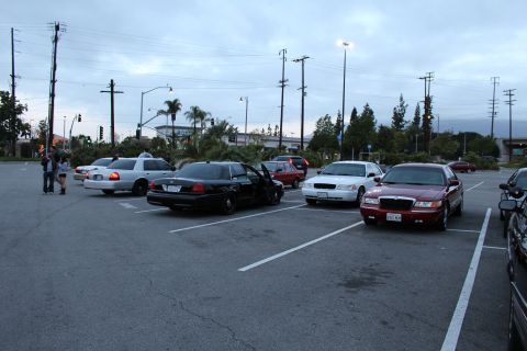 2003 Ford Crown Victoria - Several full-size sedans, including black, white and maroon cars, sit parked across a lot at dusk near power lines.