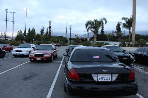 2003 Ford Crown Victoria - black Ford sedan parked at dusk shows a California plate reading 6XPD116 and a small American flag decal on the rear window.