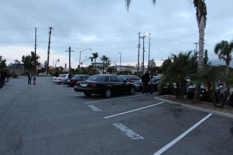 2003 Ford Crown Victoria - black full-size sedan sits angled in a parking lot at dusk as a few people stand nearby beneath a cloudy sky.