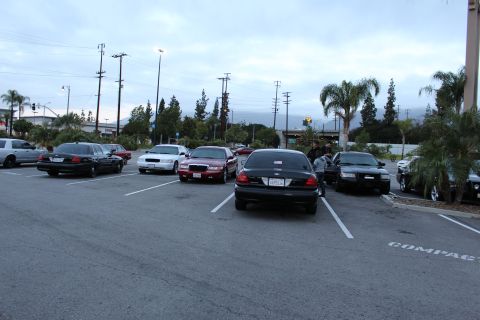 2003 Ford Crown Victoria - Several full-size sedans, including black, white and maroon cars, are parked across a lot at dusk with distant mountains.