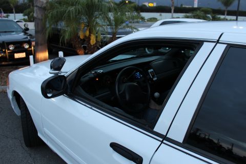 2003 Ford Crown Victoria - close side view of a white sedan reveals its steering wheel, dashboard and a mounted phone through the open windows.