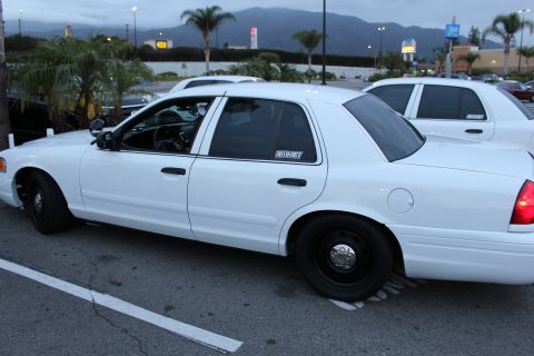 2003 Ford Crown Victoria - white Ford Crown Victoria full-size sedan with black steel wheels sits parked in a lot at dusk with mountains behind.