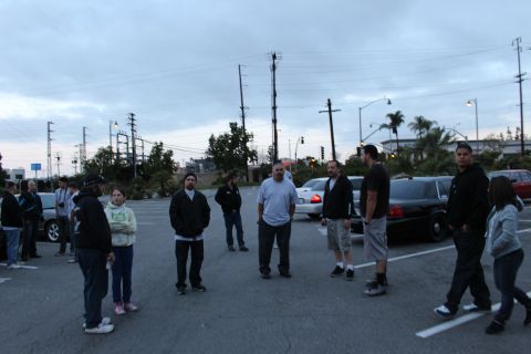 2003 Ford Crown Victoria - group of people stand and talk in a parking lot at dusk near full-size sedans under a cloudy sky.