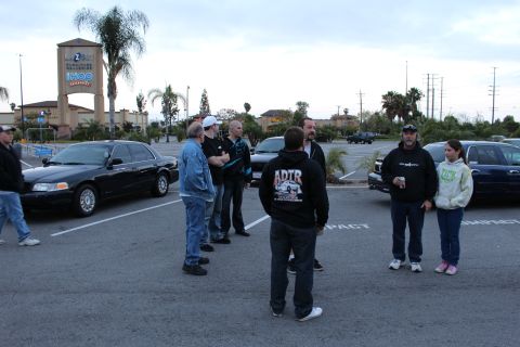 2003 Ford Crown Victoria - group of people gather in a parking lot at dusk near a black sedan, with an IHOP and shopping-center sign behind them.