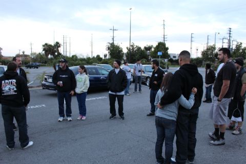 2003 Ford Crown Victoria - group of people stand in a loose circle in a parking lot at dusk with parked cars and power lines in the background.