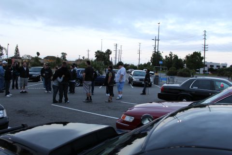 2003 Ford Crown Victoria - People stand and talk among rows of parked sedans in a cloudy-evening parking lot meet.