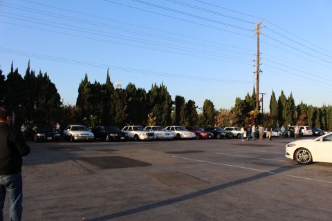 2003 Ford Crown Victoria - wide lot holds a distant row of parked sedans, with a white sedan in the foreground and a power pole behind.