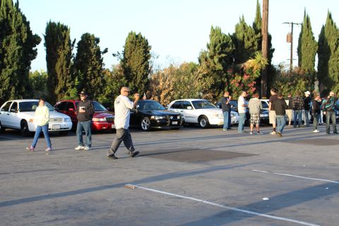 2003 Ford Crown Victoria - People walk across a parking lot past a row of parked sedans and SUVs lit by warm low-angle sun.