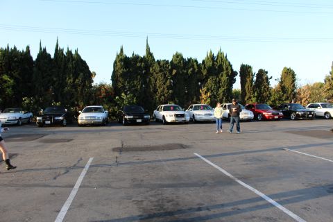 2003 Ford Crown Victoria - row of black and white sedans parks across a wide empty asphalt lot, with two people standing center.