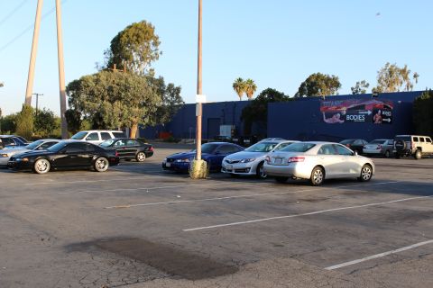 2003 Ford Crown Victoria - black coupe, blue and silver sedans park in a lot in front of a blue warehouse with a painted mural.