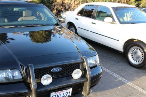 2003 Ford Crown Victoria - black Ford full-size sedan with a black push bar, fog lights and California plate 6TVL491 parked next to a white sedan with chrome wheel co…