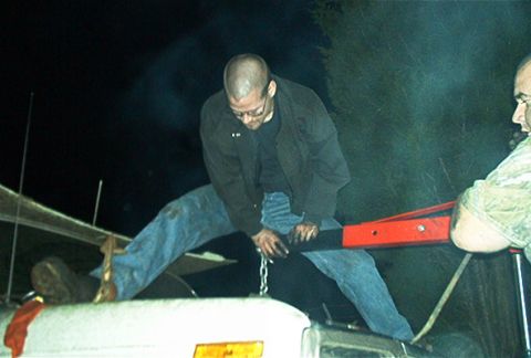 1979 Ford Bronco - Two men use an engine hoist to lift an engine over a white vehicle in the dark.
