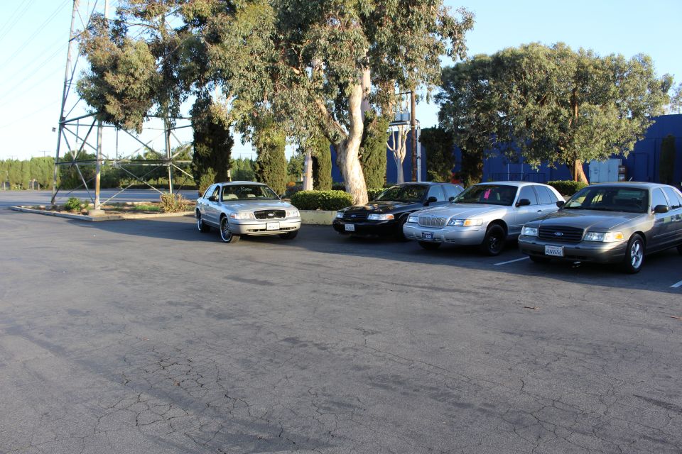 Silver, black, and white Ford sedans parked in a lot by a blue building