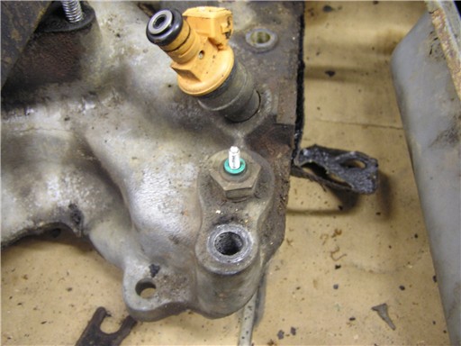 Yellow fuel injector seated in a cast aluminum lower intake manifold on a shop floor