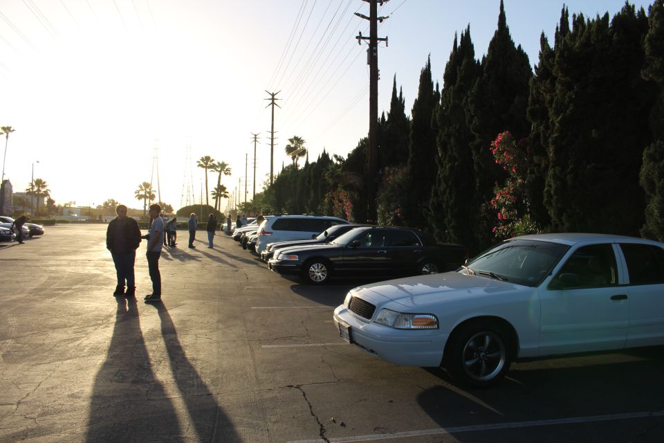 White Ford Crown Victoria in a parking lot with people casting long shadows in low sun