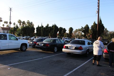 2003 Ford Crown Victoria - white SUV and a silver Ford sedan sit among parked cars in a sunlit lot as a person stands at right beside the row.