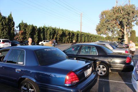 2003 Ford Crown Victoria - dark blue Crown Victoria with a club window decal sits beside black Ford sedans at an outdoor enthusiast gathering.