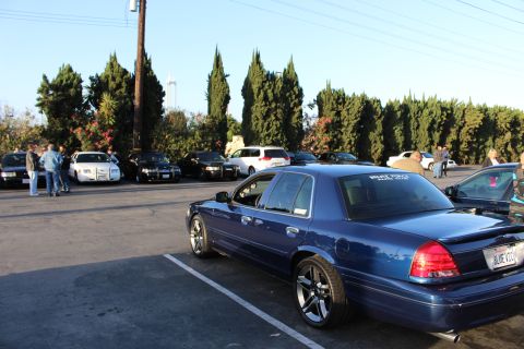 2003 Ford Crown Victoria - dark blue Ford Crown Victoria sedan in the foreground of a parking-lot meet, with rows of full-size sedans behind.