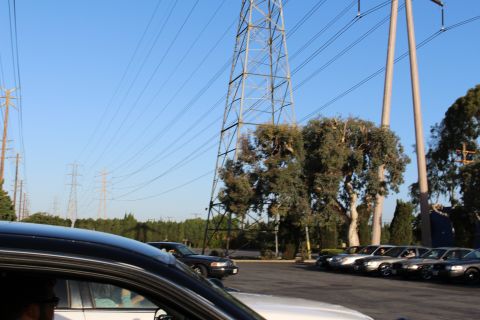 2003 Ford Crown Victoria - Tall steel transmission towers and power lines tower over a parking lot of sedans, with a dark car cropped in the foreground.