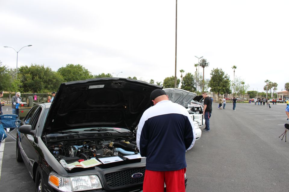 Man in white jacket looking under the hood of a black sedan at a meet