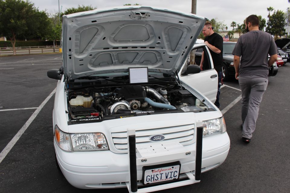 White Ford with open hood and personalized plate GHST VIC at a car meet