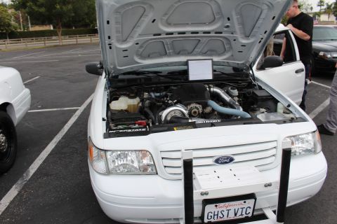 2003 Ford Crown Victoria - Front view of a white Ford with raised hood revealing a turbocharged engine, personalized plate GHST VIC at the parking lot meet.