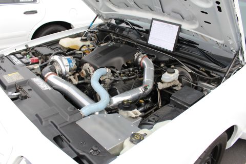 2003 Ford Crown Victoria - Close-up of a turbocharged V engine in a white car with polished intercooler piping and a printed sheet propped on the strut tower.