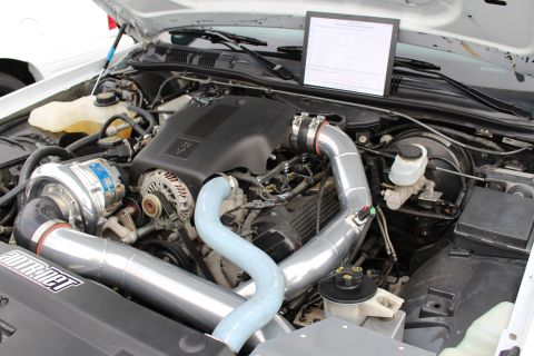 2003 Ford Crown Victoria - detailed turbocharged engine fills a white car's bay, with chrome intercooler piping, a turbo unit, and a judging sheet on the cowl.
